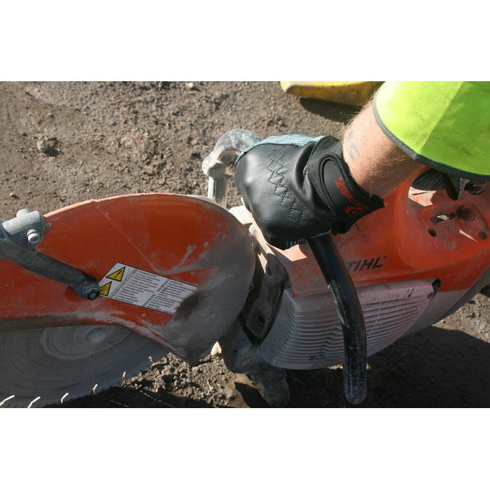 A close-up action shot of a person wearing a black predator-branded work glove while operating a red and silver STIHL circular saw on dirt ground.