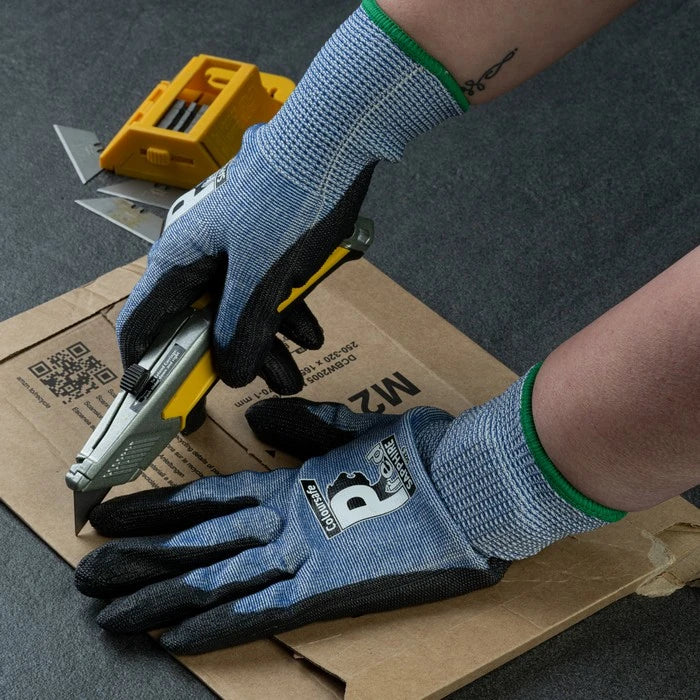 Person wearing gloves using a box cutter on cardboard
