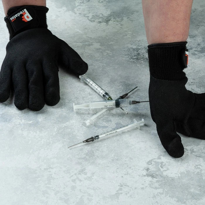 Black work gloves with a visible red and white 'Predator' logo on the wrist cuff, worn on hands with three medical syringes on a gray stone-textured surface.