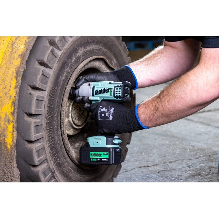 A person wearing black gloves uses a cordless impact wrench to loosen a lug on a rugged off-road tire in an outdoor setting.