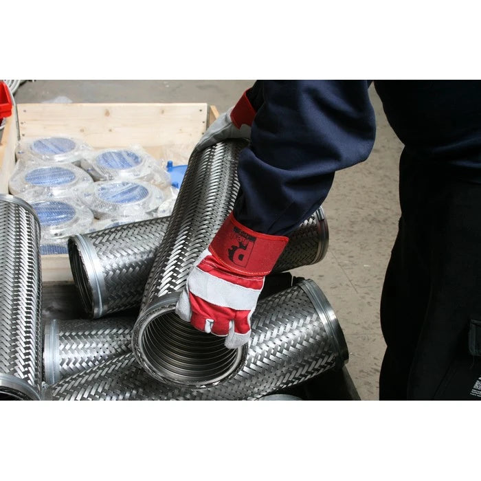 A person wearing a navy blue work jacket and red-and-white protective gloves handles a coiled metallic corrugated pipe or hose in a workshop setting.